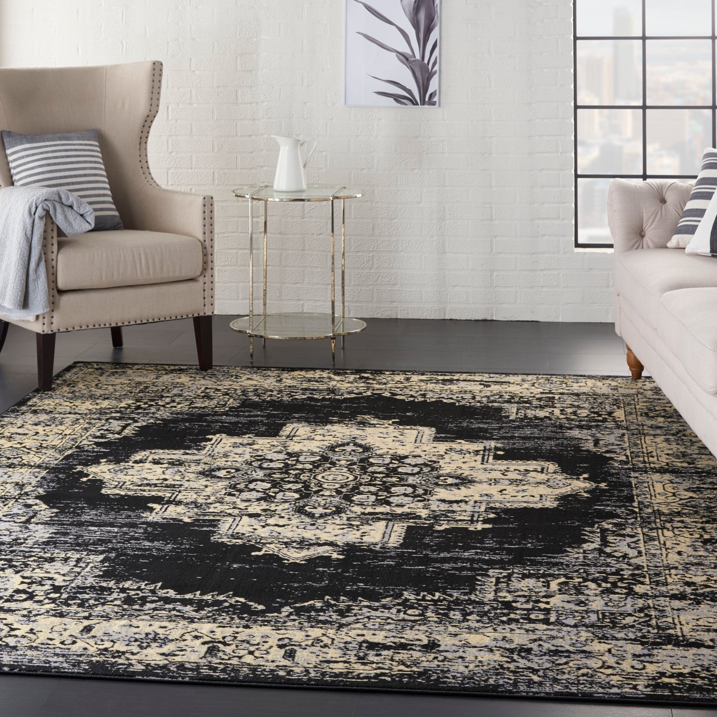 Beige upholstered armchair and sofa with striped cushions, gold side table, white brick wall, and a black-and-cream rug.