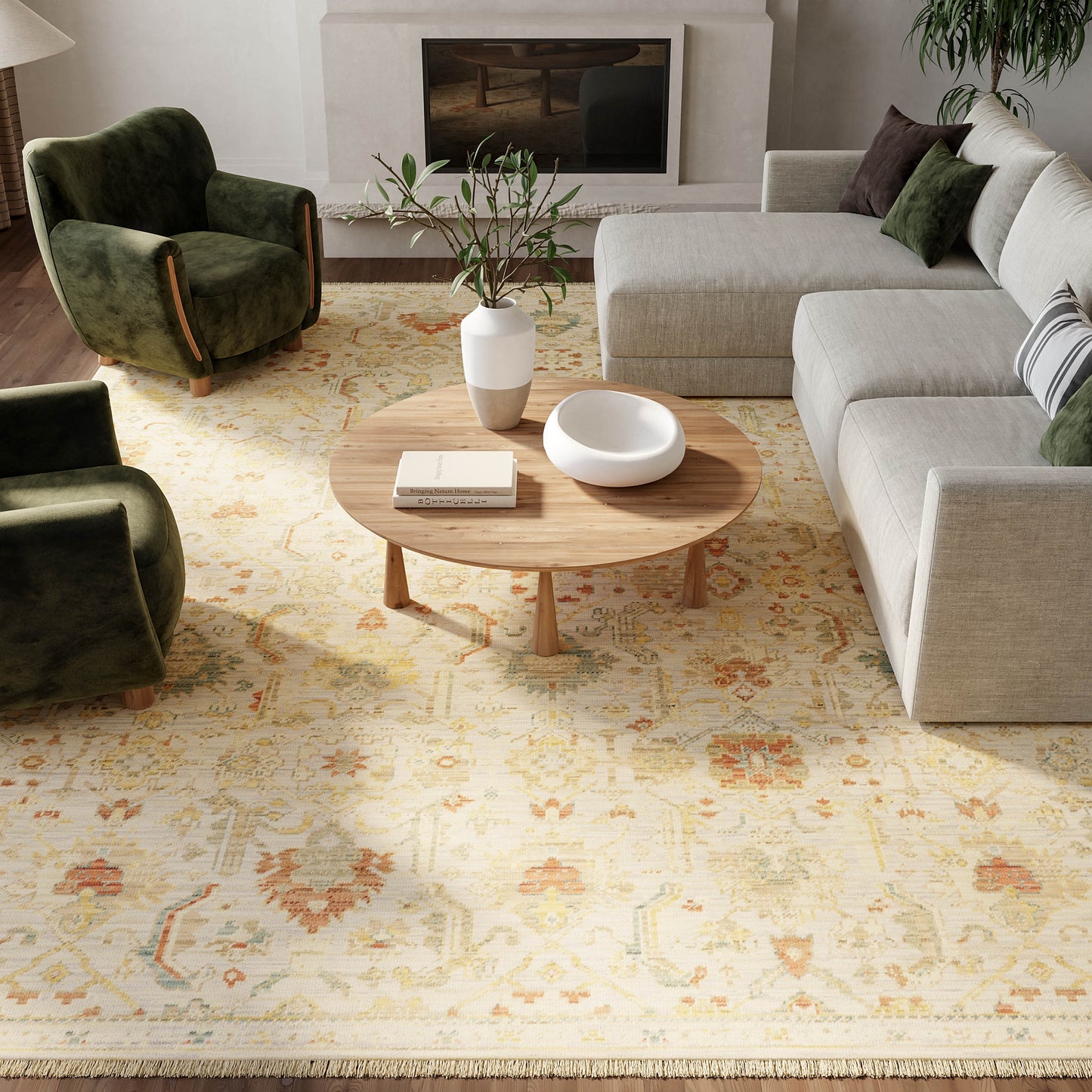 Round wooden coffee table on a cream floral rug, flanked by gray sectional and green velvet chairs in a modern living room.