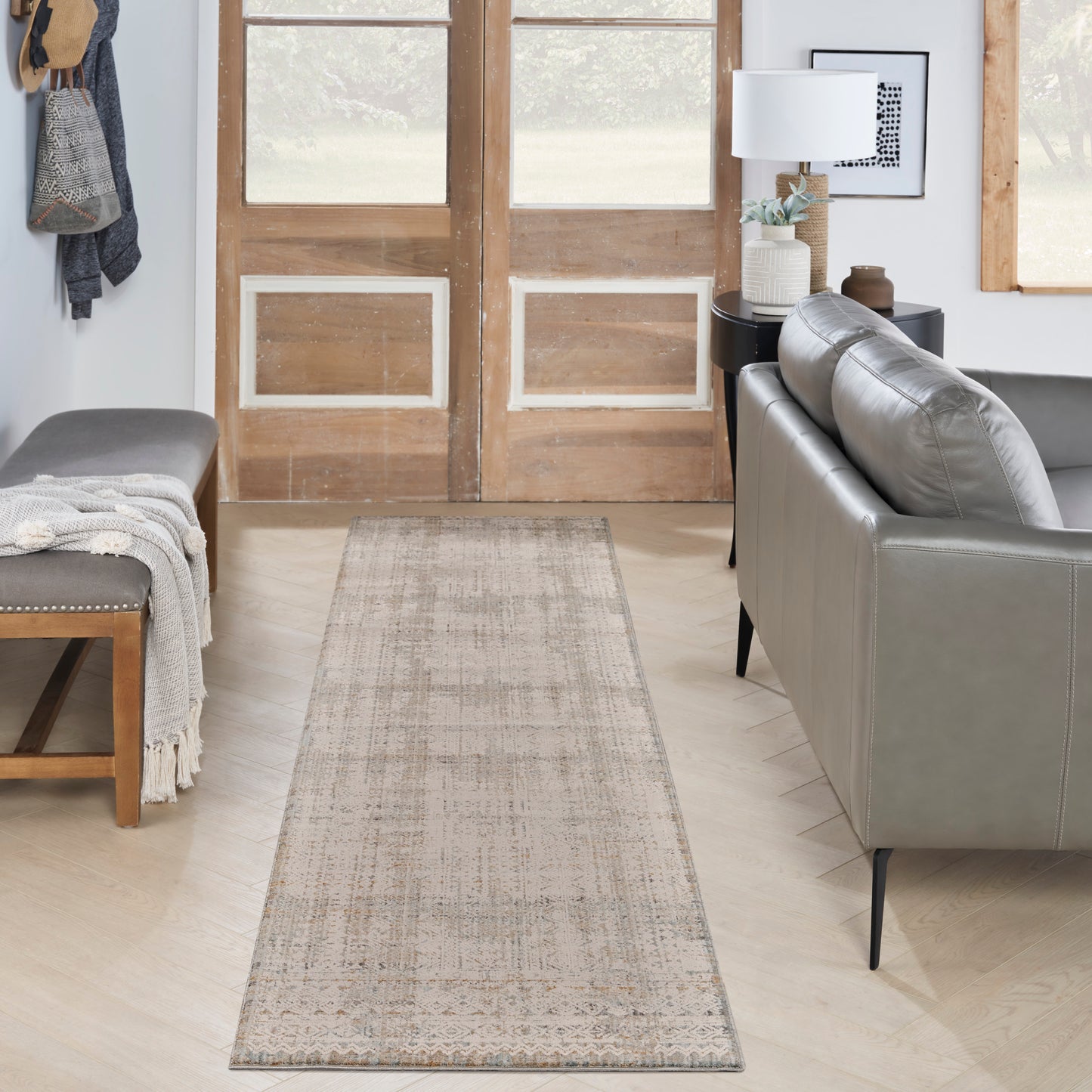 Beige woven runner rug on light wood floor between a gray leather sofa and an entry bench with a throw blanket.