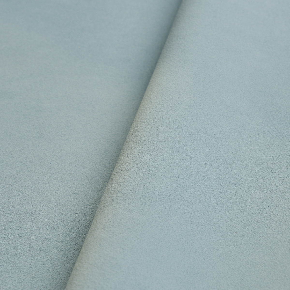 Powder-blue suede-textured fabric with a diagonal fold, soft and plush, suitable for upholstery or crafts.