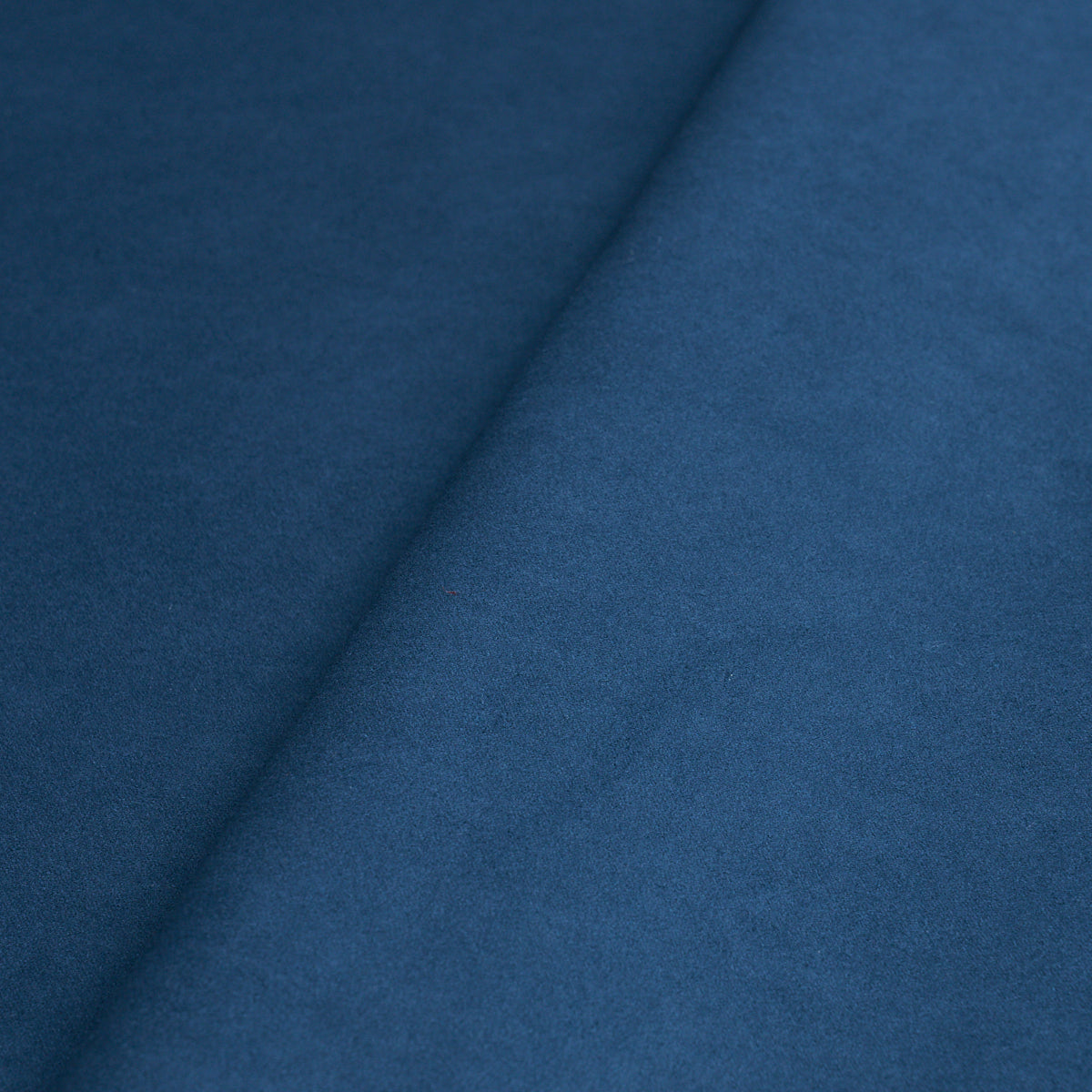 Cobalt blue suede-like fabric close-up with a diagonal fold and soft nap.