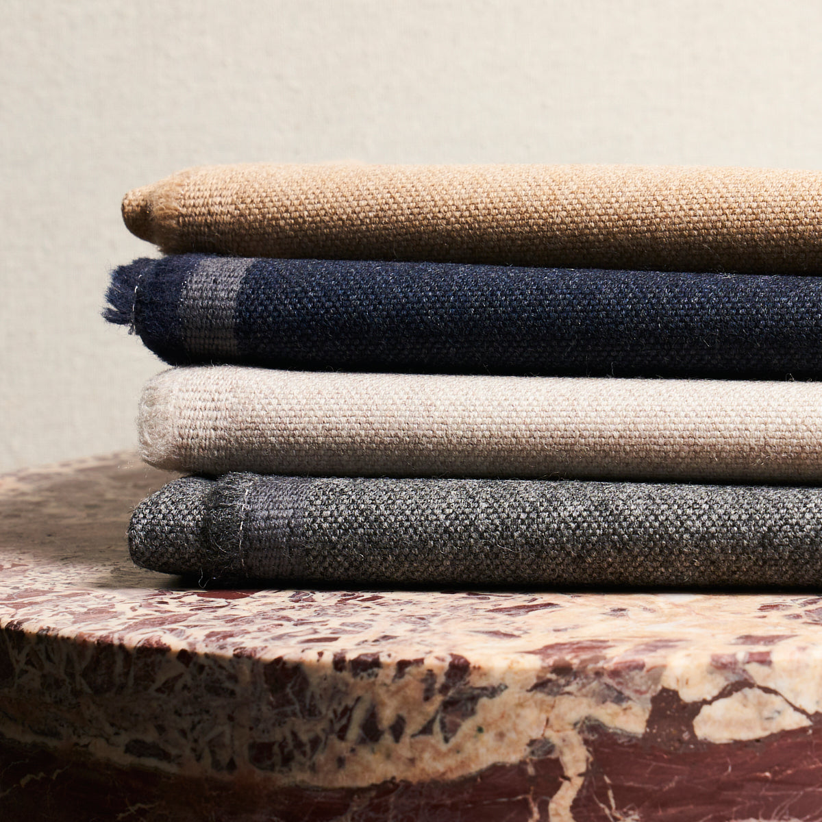 Stack of folded woven blankets in tan, navy, beige, and gray on a marble table.