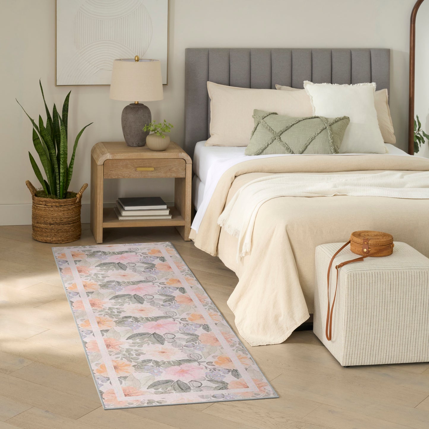 Neutral bedroom with beige linen bedding, gray tufted headboard, wooden nightstand, potted plant, pastel patterned runner rug.