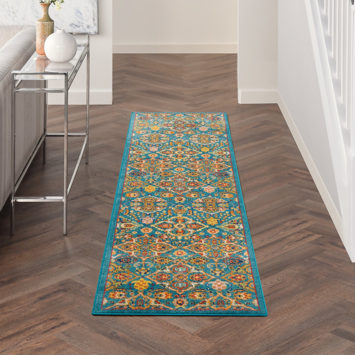 Long turquoise-bordered oriental runner rug with teal, orange and yellow motifs in a dark wood hallway.