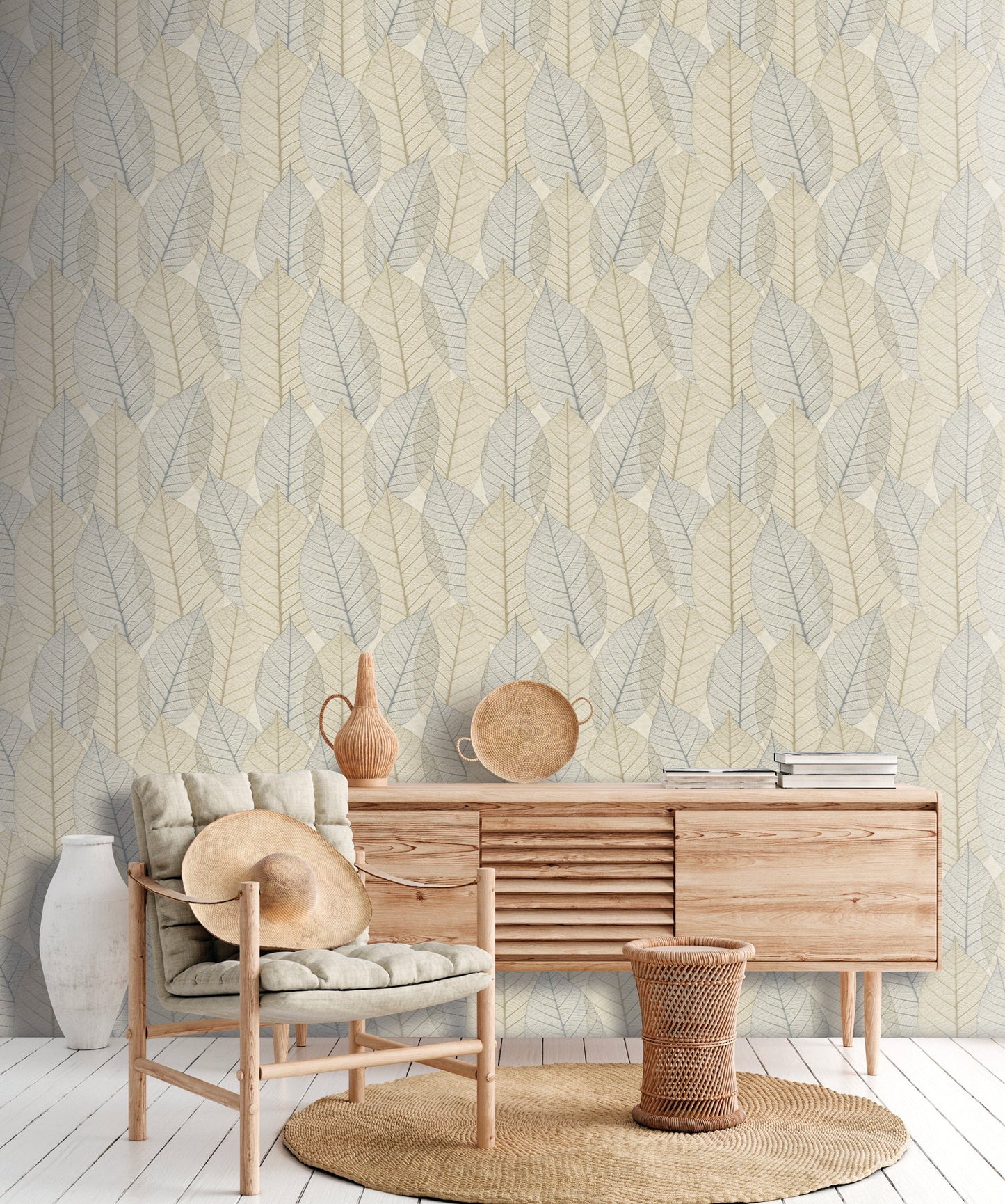 Leaf Lace blue beige wallpaper on a wall behind a living room scene featuring a mid-century wooden sideboard, a cushioned lounge chair, a round jute rug, a ceramic vase & a woven basket.
