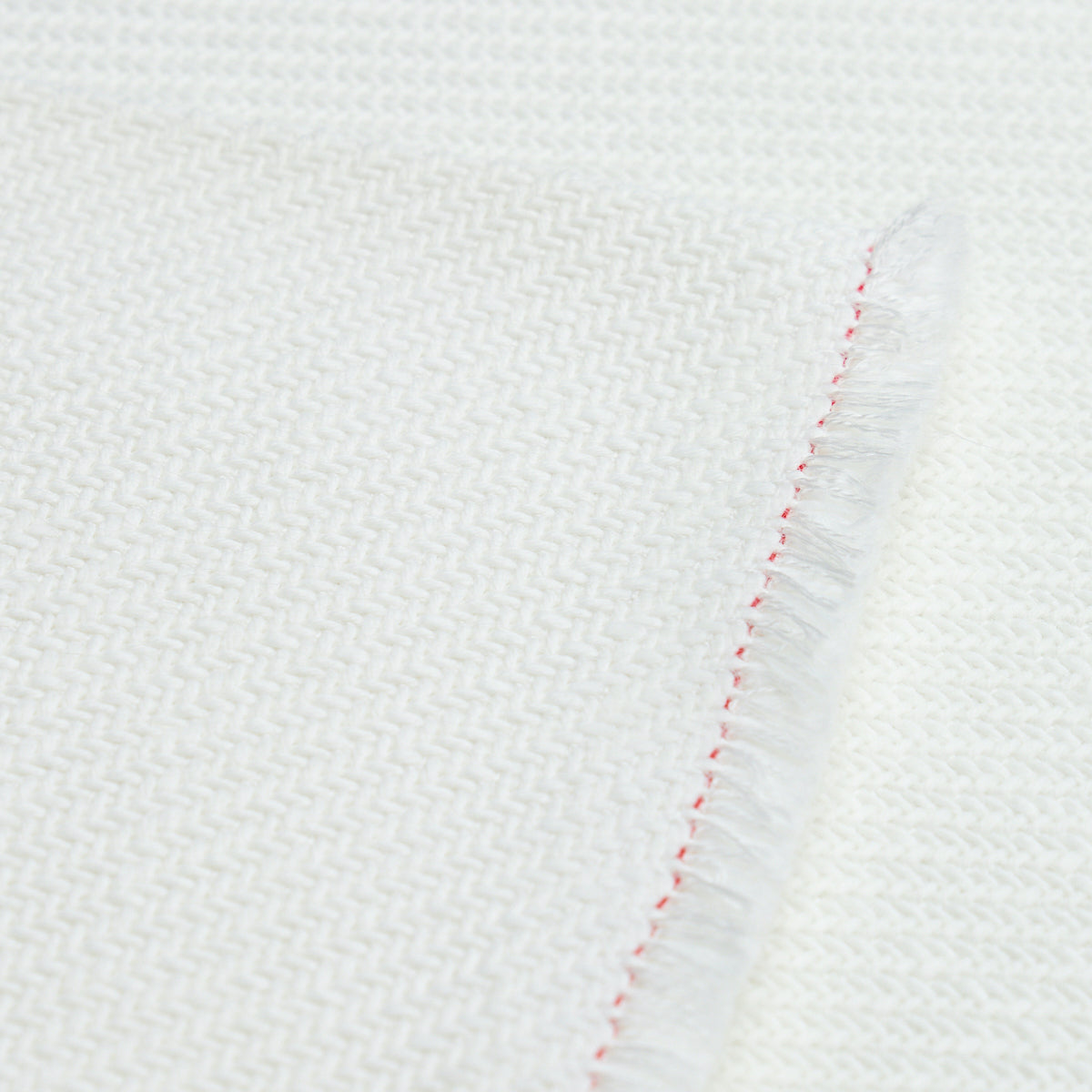 White woven textile with herringbone pattern, folded edge with red stitching and fringe detail.