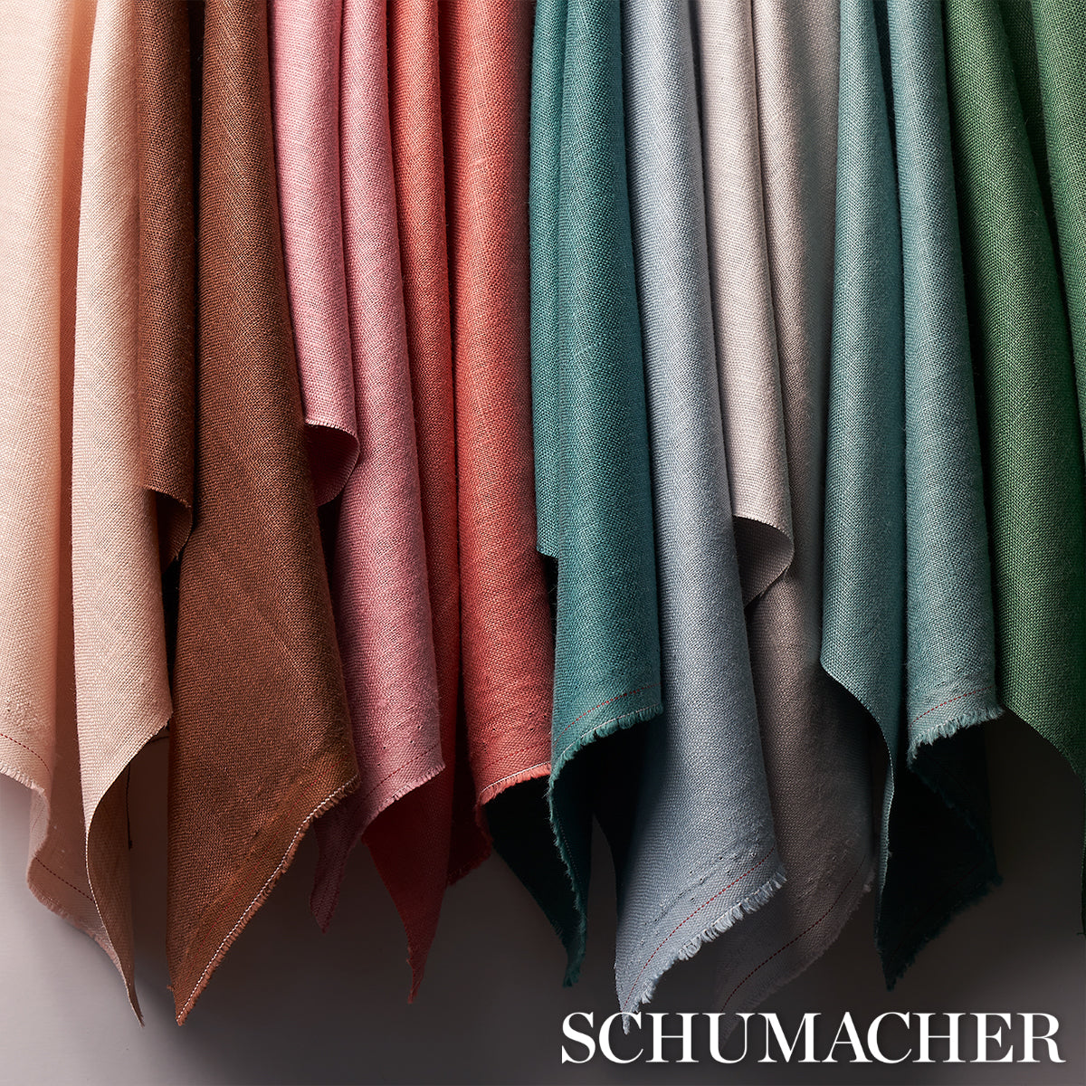 Rows of suede-like fabric swatches hanging side by side in warm to cool tones with fringed edges; Schumacher watermark.