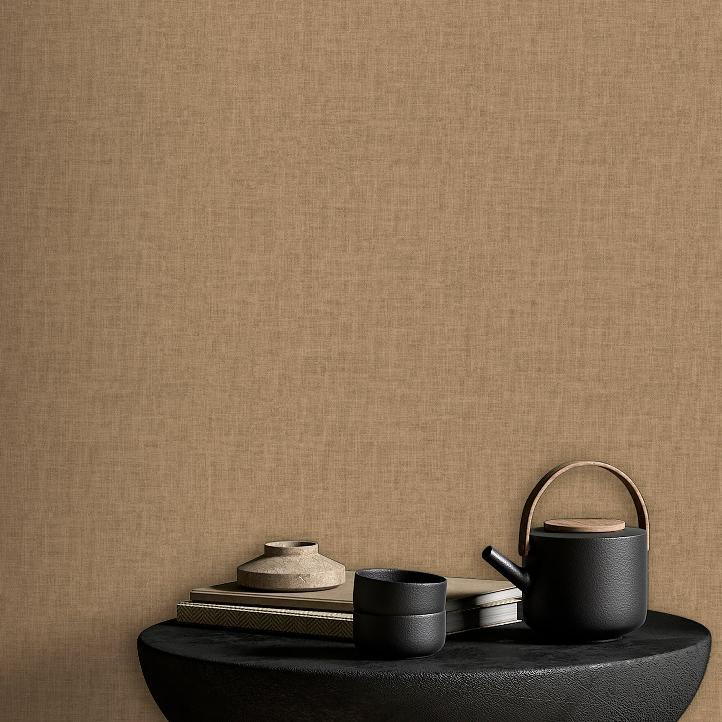 Beige textured wall backdrop with a black teapot, two cups, & a stack of books on a rounded black table.