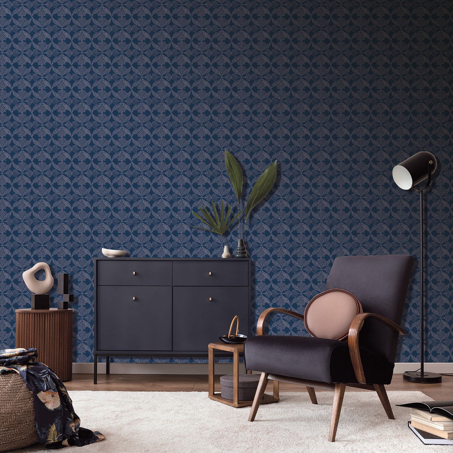 Mid-century navy armchair with wooden arms beside a navy sideboard, plant, & tall floor lamp against blue wallpaper.