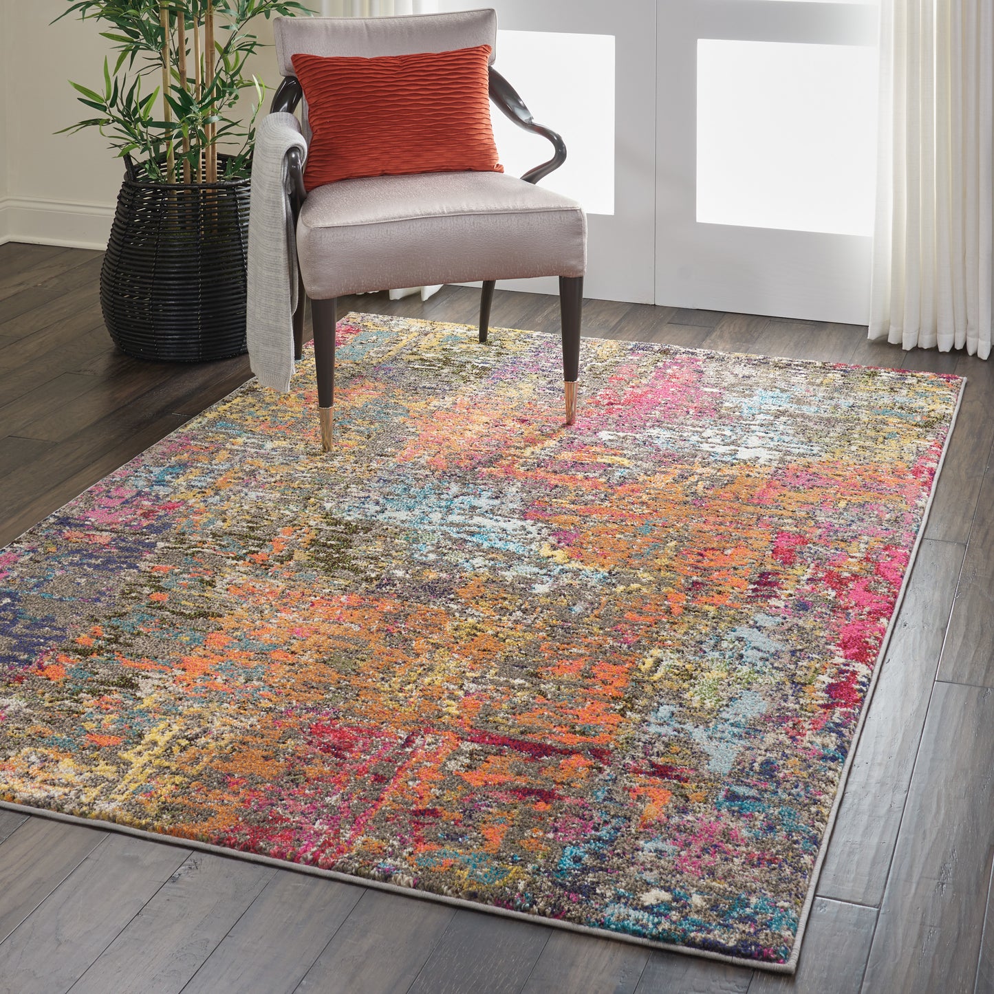 Colorful abstract rug over dark wood floor under a beige upholstered chair with an orange textured pillow.