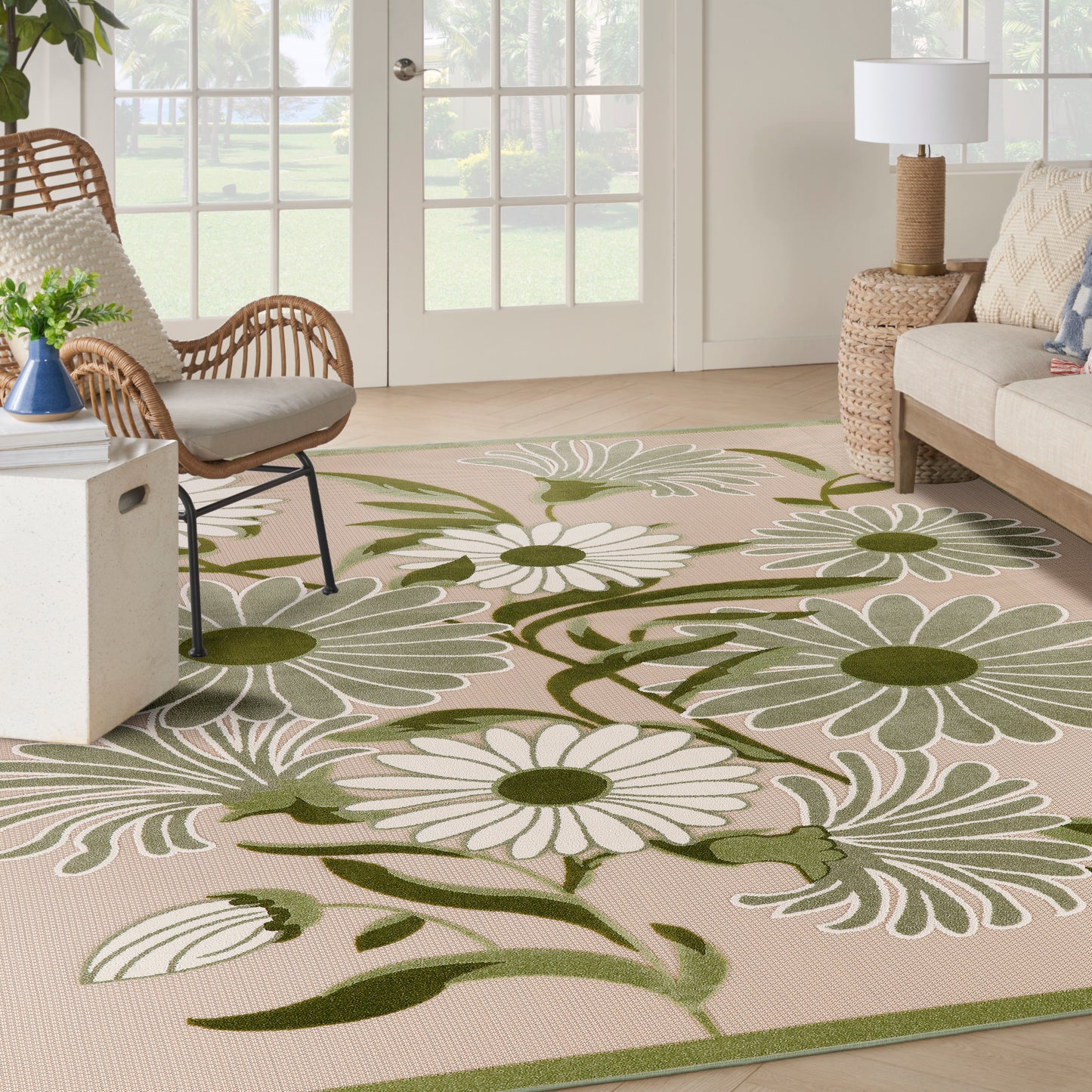 Beige outdoor rug with oversized white daisies & olive-green stems; coastal living room with wicker chair & sofa.