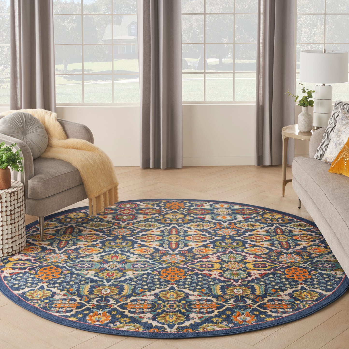Round navy rug with vivid multicolor floral medallion pattern in a living room with gray sofa, curtains, and wooden floor.