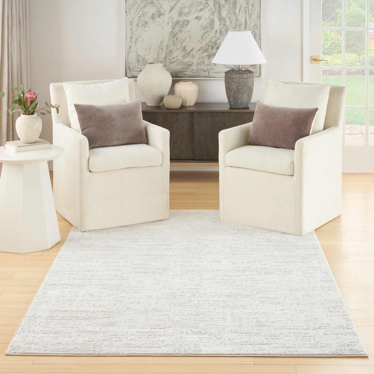 Two cream fabric armchairs & taupe pillows around a light gray textured area rug in a modern living room.