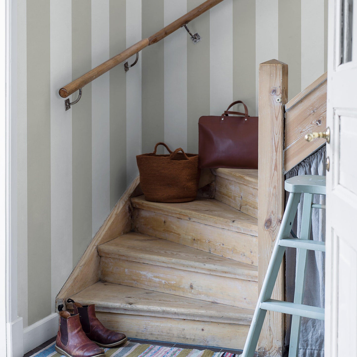 Rustic wooden staircase with pale striped walls; burgundy leather handbag and woven basket on steps, brown boots at base.