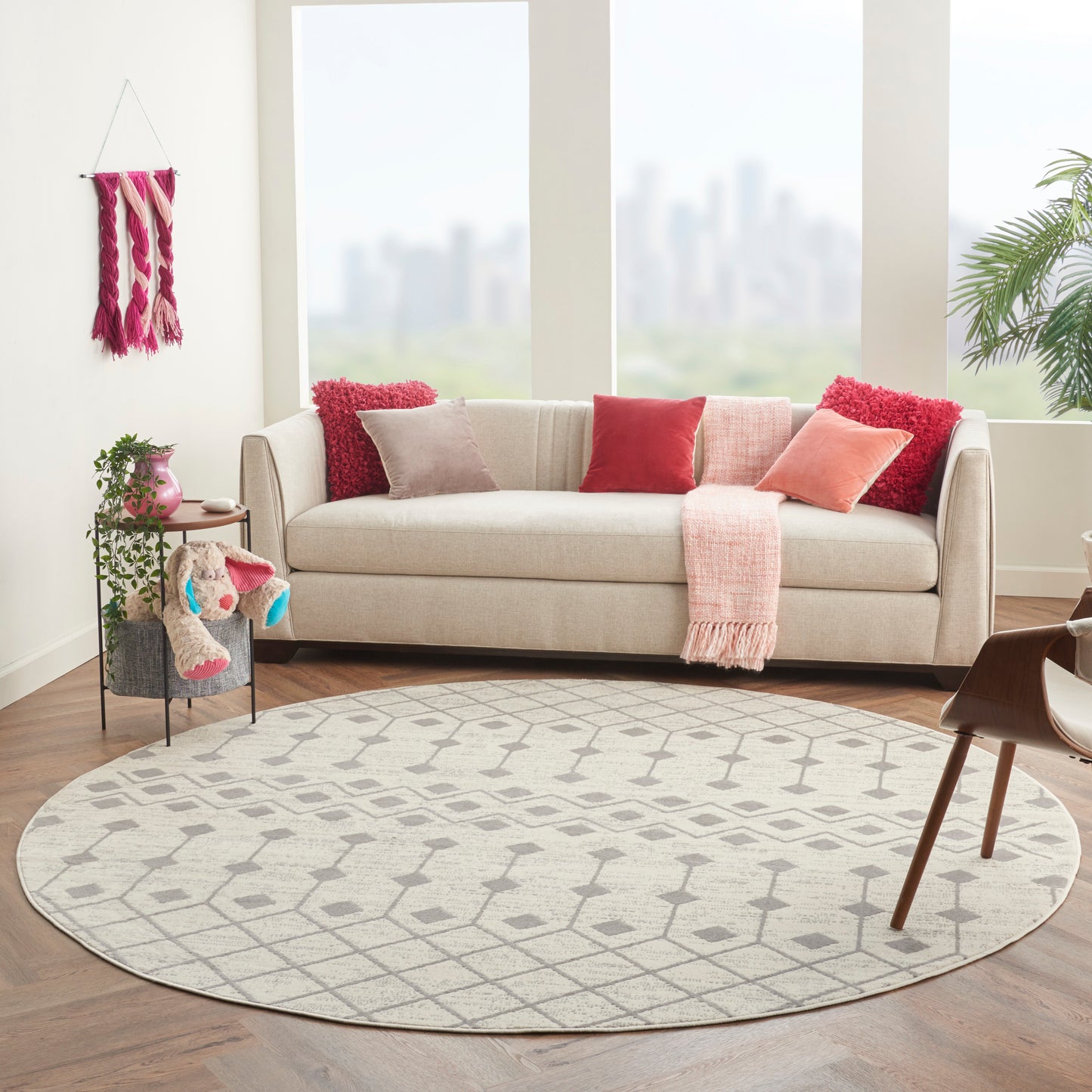 8' round bohemian geometric rug in a sunlit living room with a beige fabric sofa, pink accents, and houseplants.
