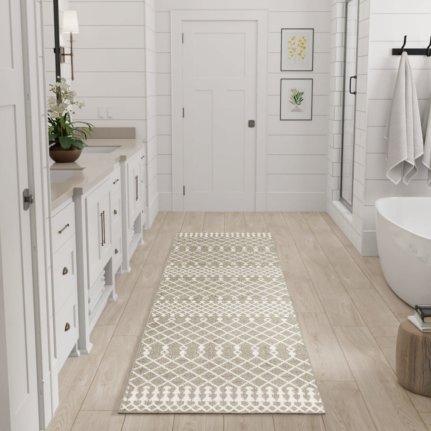 Long beige and white geometric rug runner in bright bathroom with white cabinetry, potted plant, tub & glass shower.