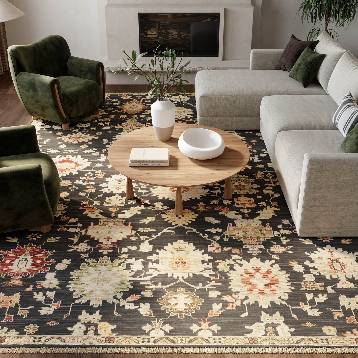 Living room with a floral patterned rug, light gray sectional, dark green velvet chairs, round wood coffee table, vase.