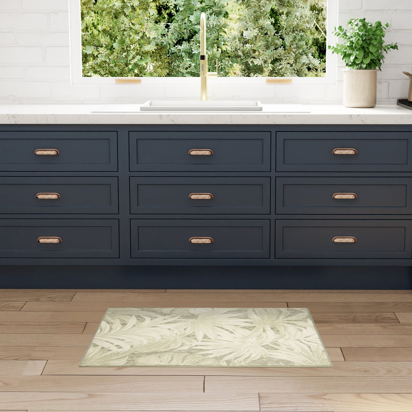 Navy blue kitchen cabinets with copper handles, white quartz countertop, gold faucet, pale green leafy rug on wood floor.