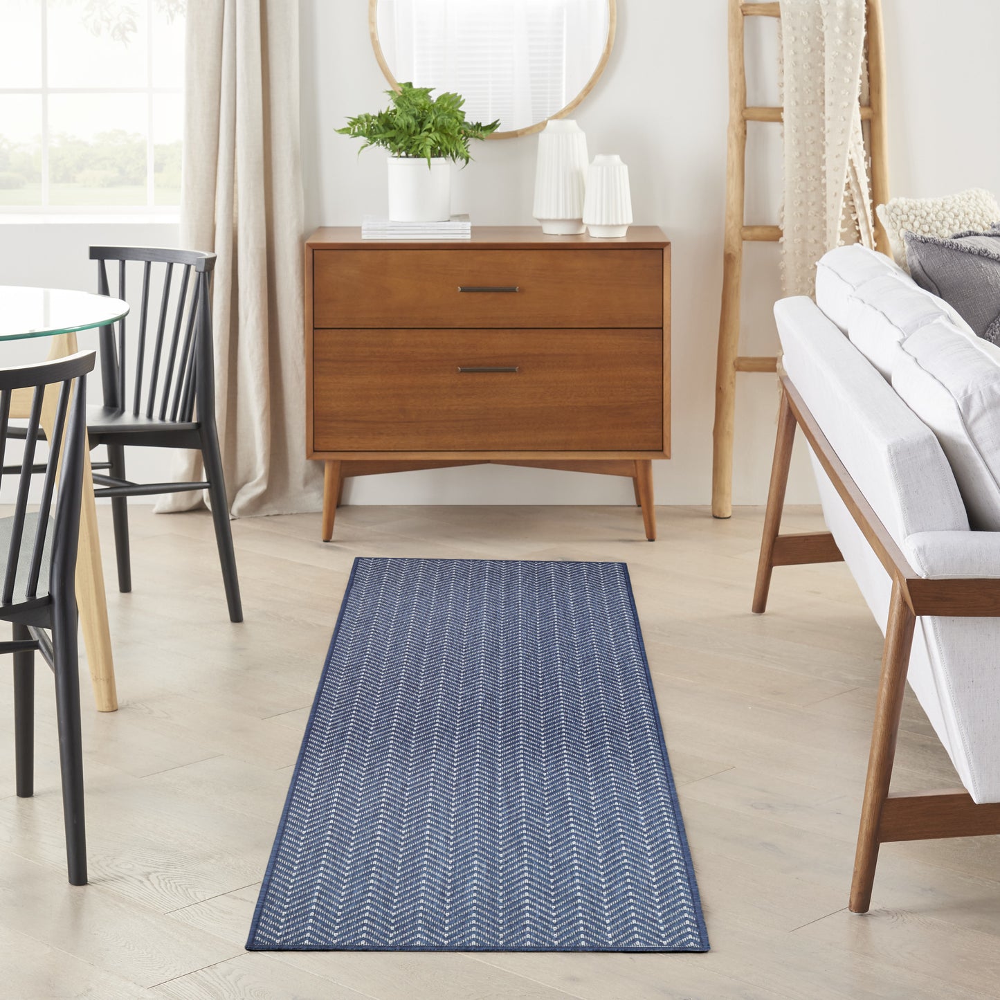 Navy blue chevron runner rug laid on light wood floor in a mid-century living room with a wood dresser, sofa, and ladder.