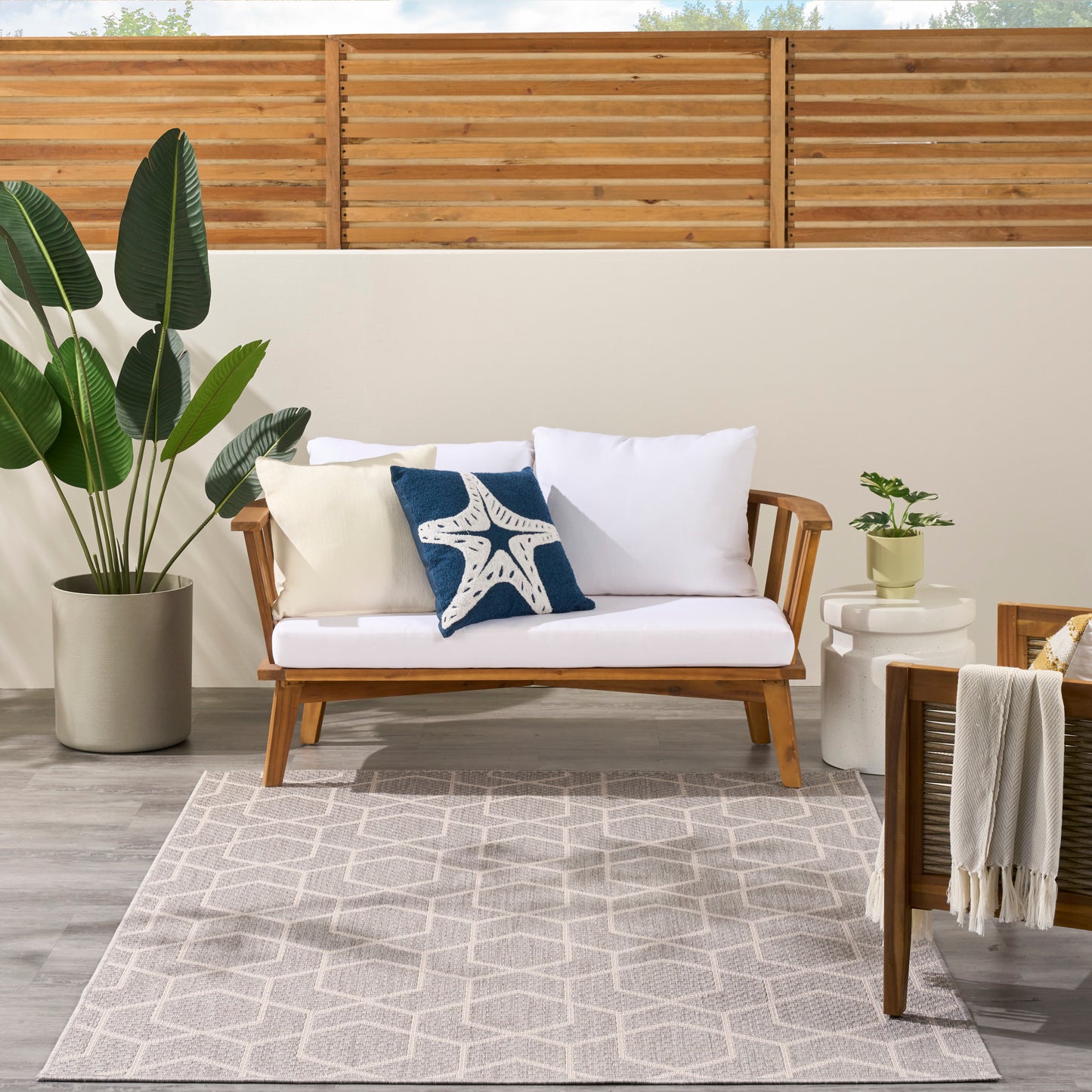 Modern 5' x 7' geometric outdoor rug in a coastal patio setting with plants.