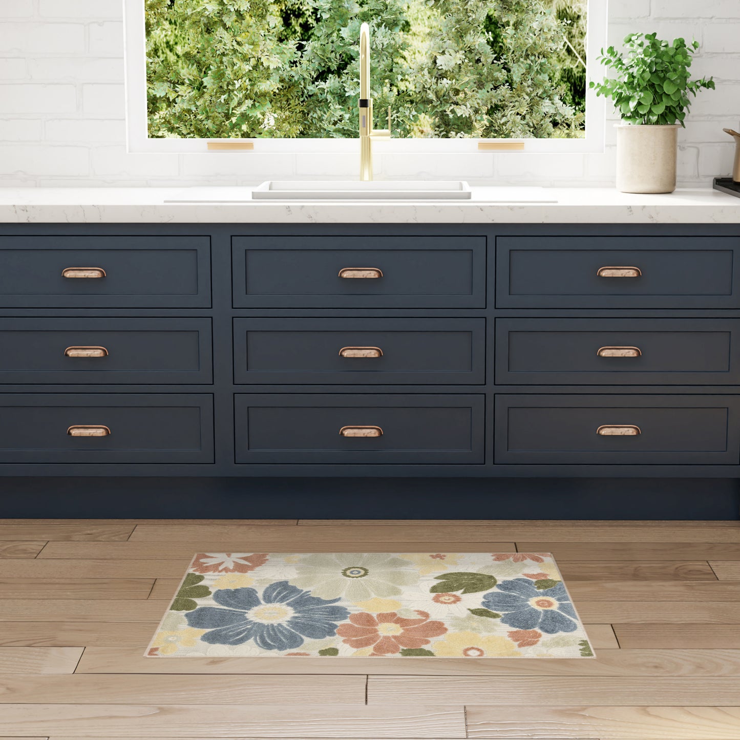 Navy blue kitchen cabinets & copper pulls, white marble countertop, gold faucet, window view; floral rug on wood floor.