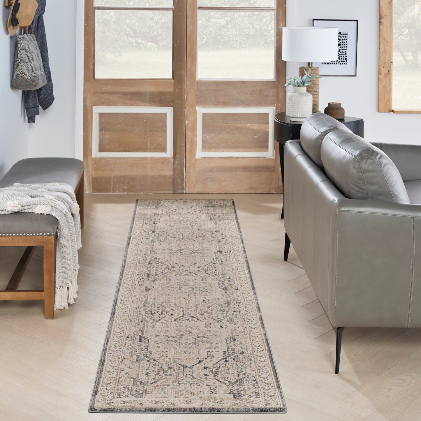 Beige traditional-patterned runner rug with muted border in entryway beside gray sofa and wooden doors.
