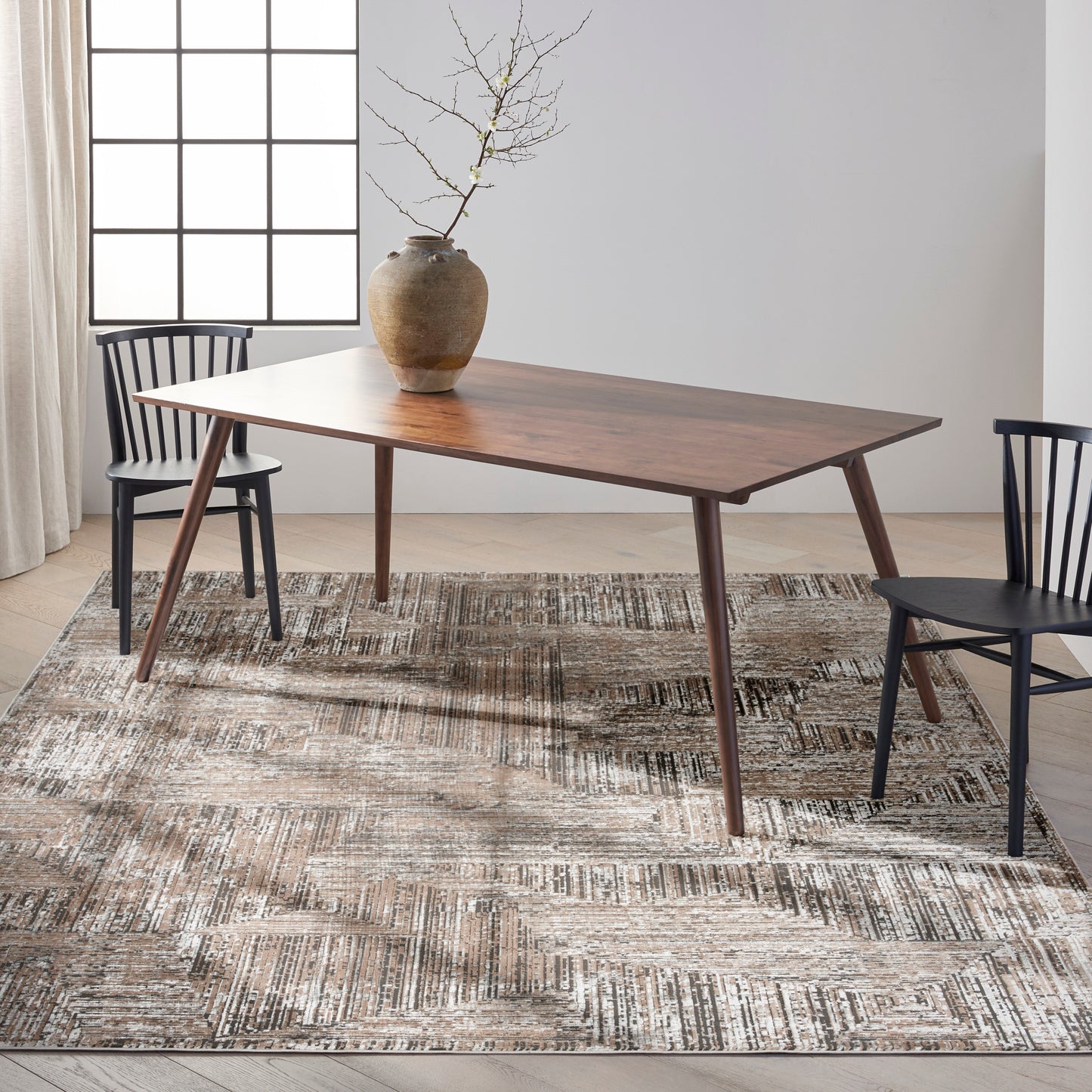 Mid-century wooden dining table with tapered legs, paired with black chairs, ceramic vase centerpiece on a textured beige rug.