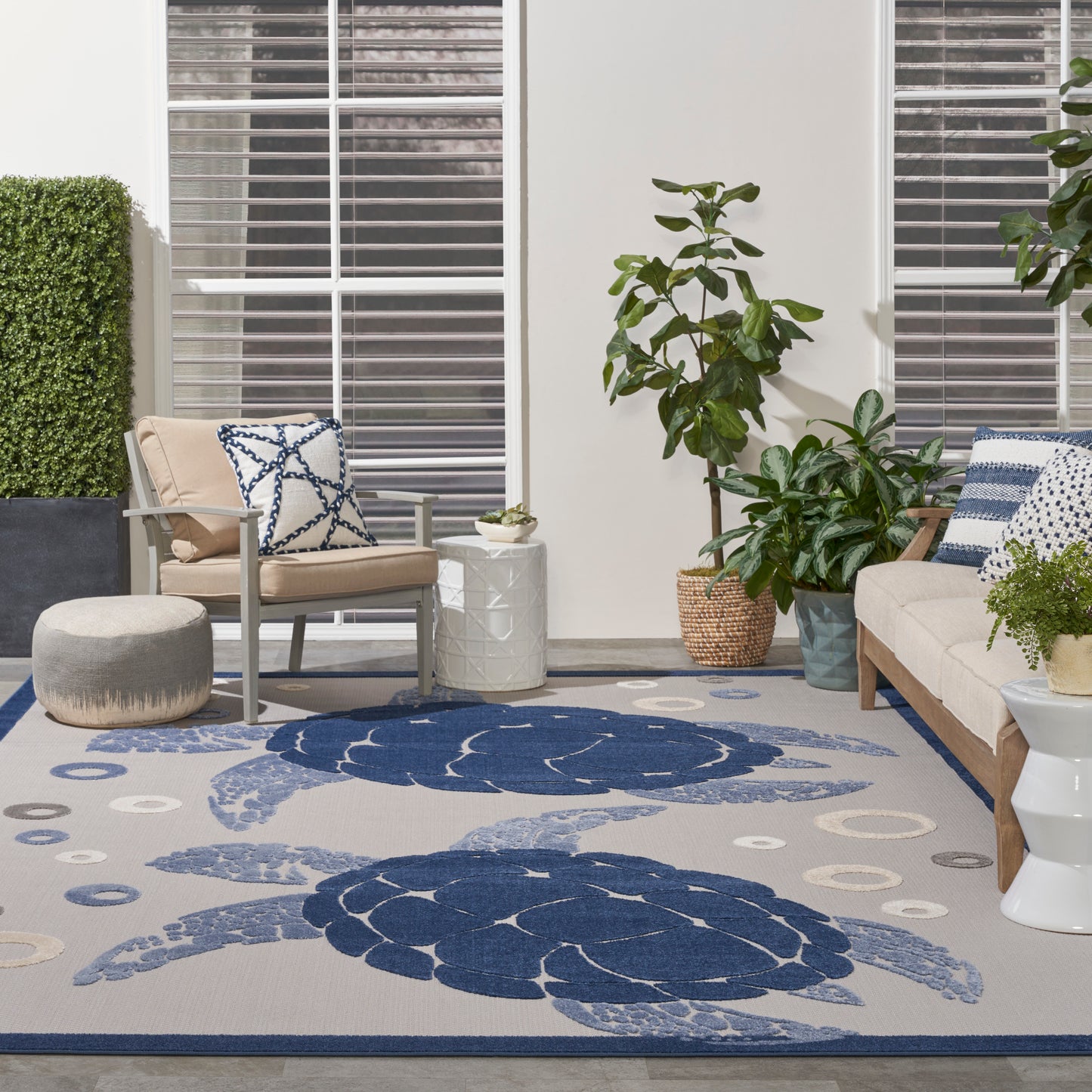 Gray rug with large navy circular patterns in an outdoor patio setting; beige seating, blue cushions, and potted plants nearby.