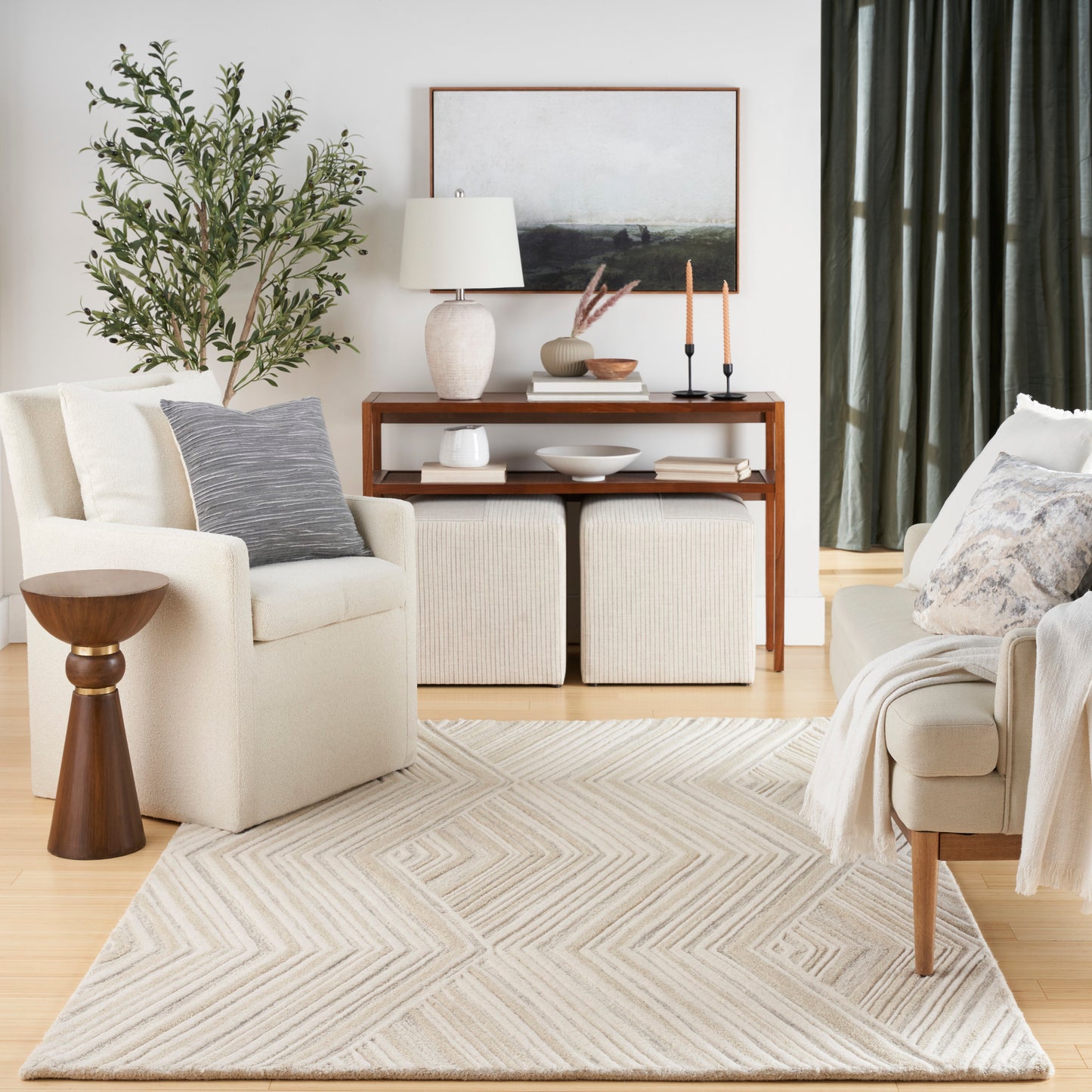 Beige living room with cream chairs, chevron rug, wooden console, lamp, plant, and gray pillows.