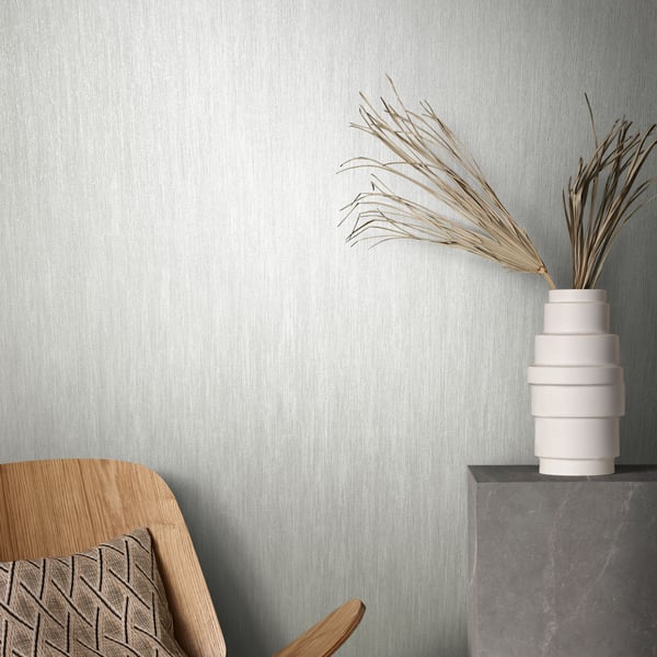 Neutral interior corner with white wallpaper on the walls; wooden chair with a patterned cushion and a stacked white vase with dried pampas grass on a concrete pedestal.