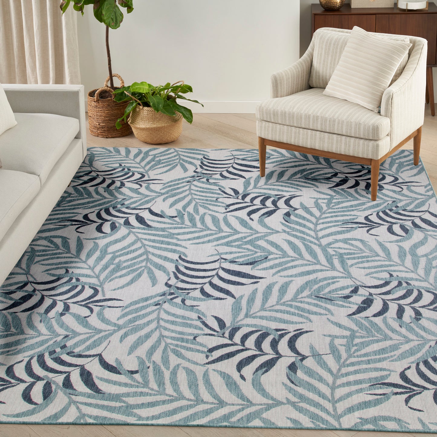 Living room corner with teal navy leaf-pattern rug, beige sofa, striped armchair, and woven plant baskets.