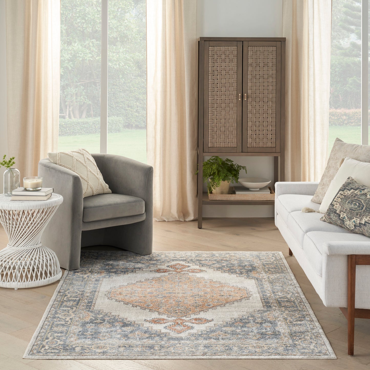 Cozy living room with gray armchair, white woven side table, cane-panel cabinet, light sofa, and blue-gray geometric rug.