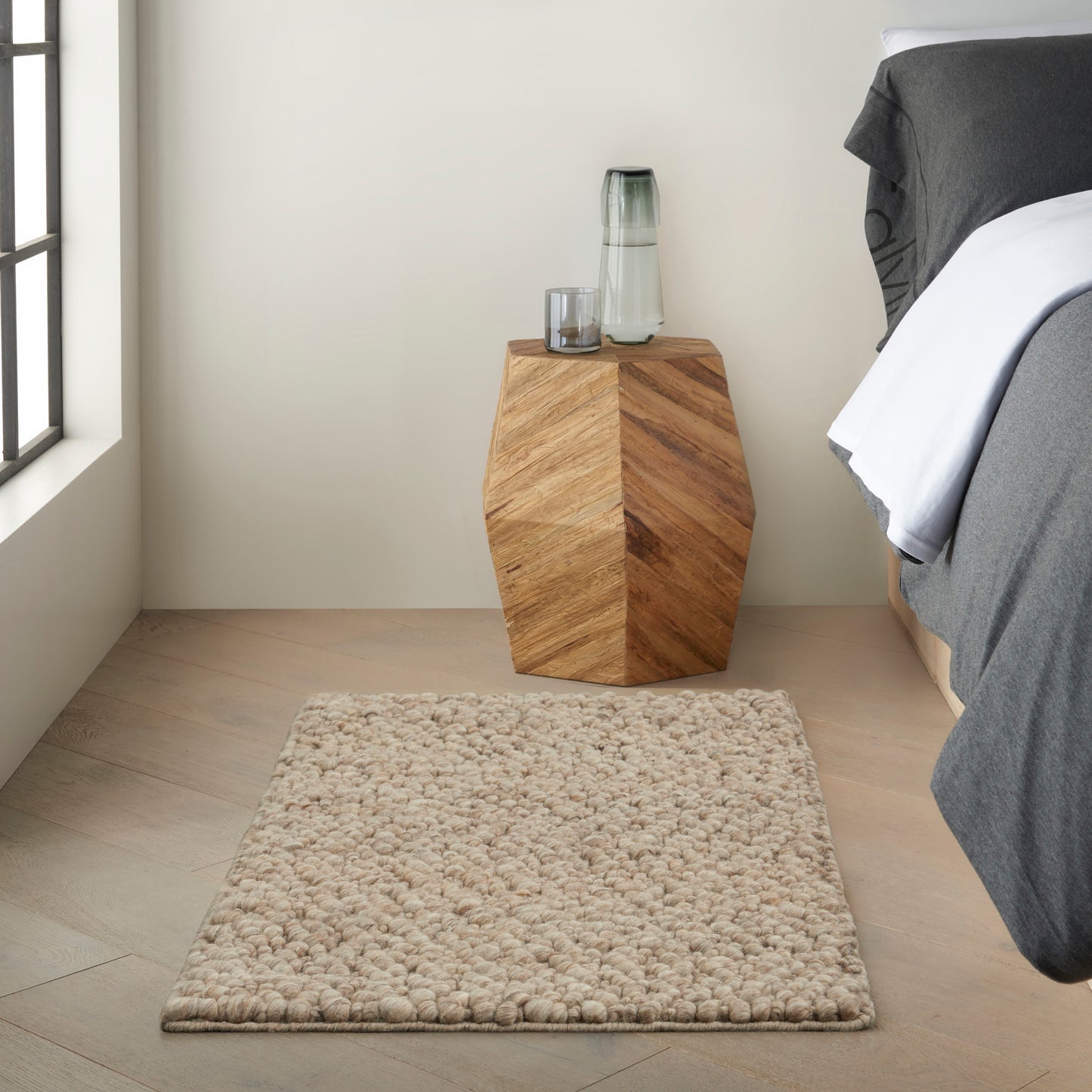 Beige shag rug on light wood floor in a simple bedroom scene.