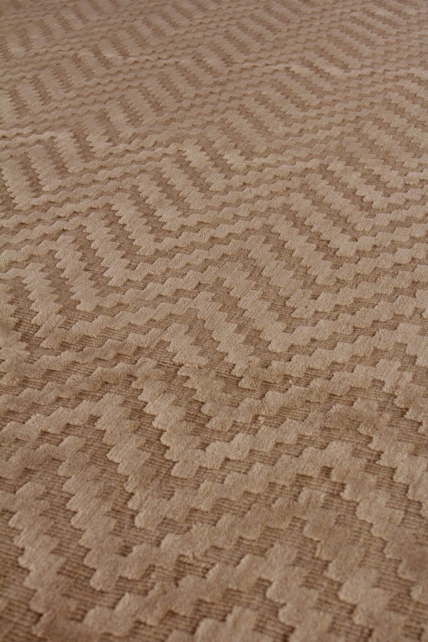 Beige textured rug with repeating zigzag chevron pattern in tan tones.