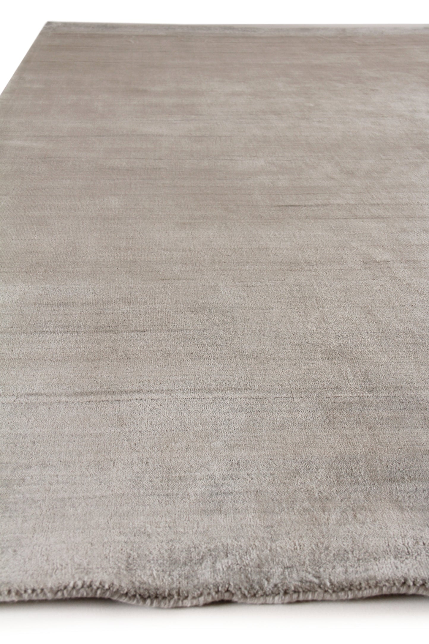 Taupe/greige low-pile area rug with soft texture, subtle shading and fringe along edge.
