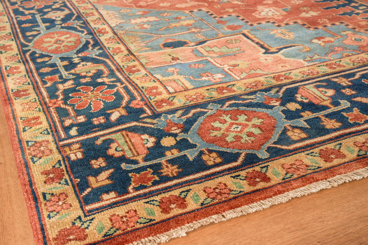 Colorful oriental rug with blue & navy field, red & gold borders, floral medallions & fringe on a wooden floor.