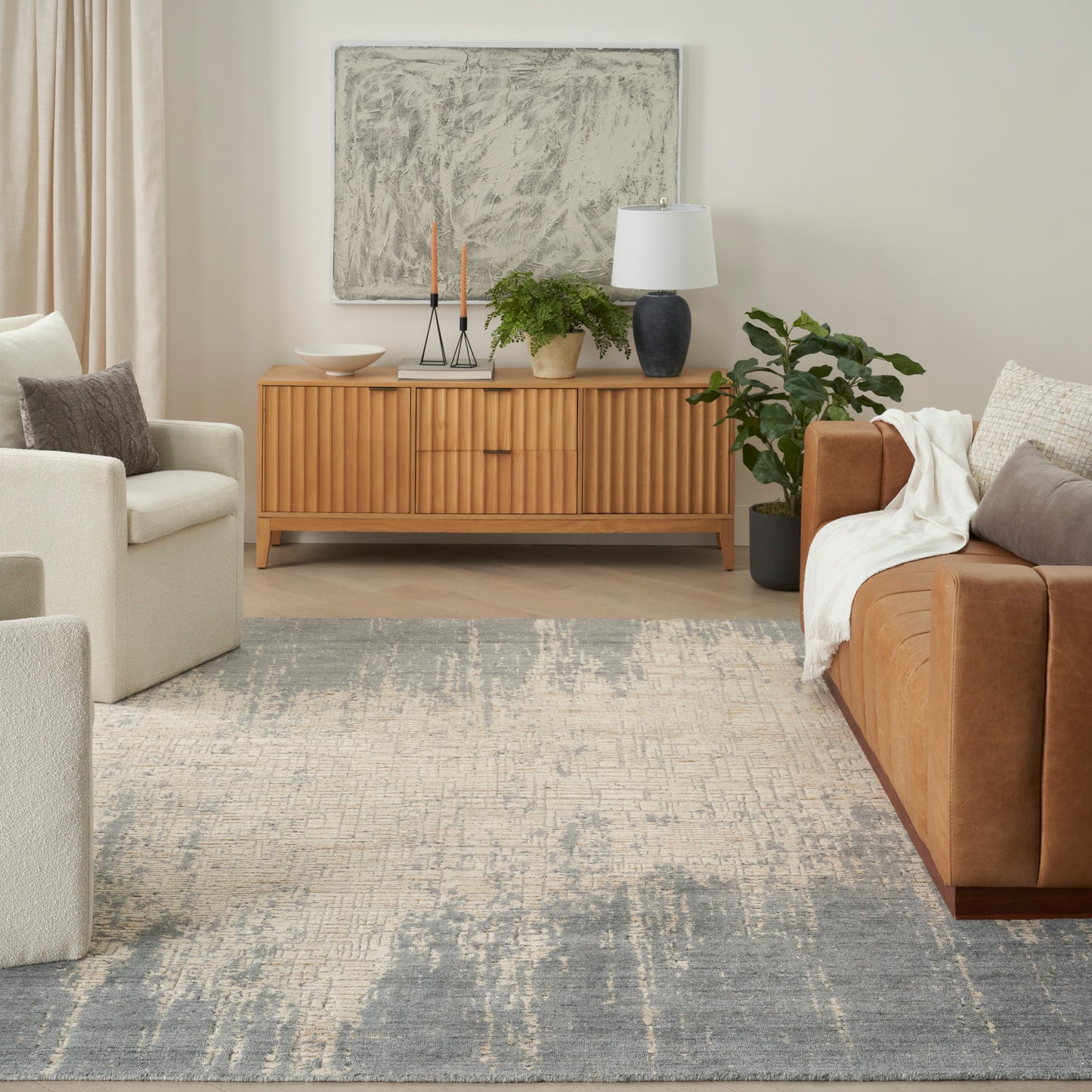 Neutral living room with mid-century wooden sideboard, abstract art, gray rug, beige chairs, and a brown leather sofa