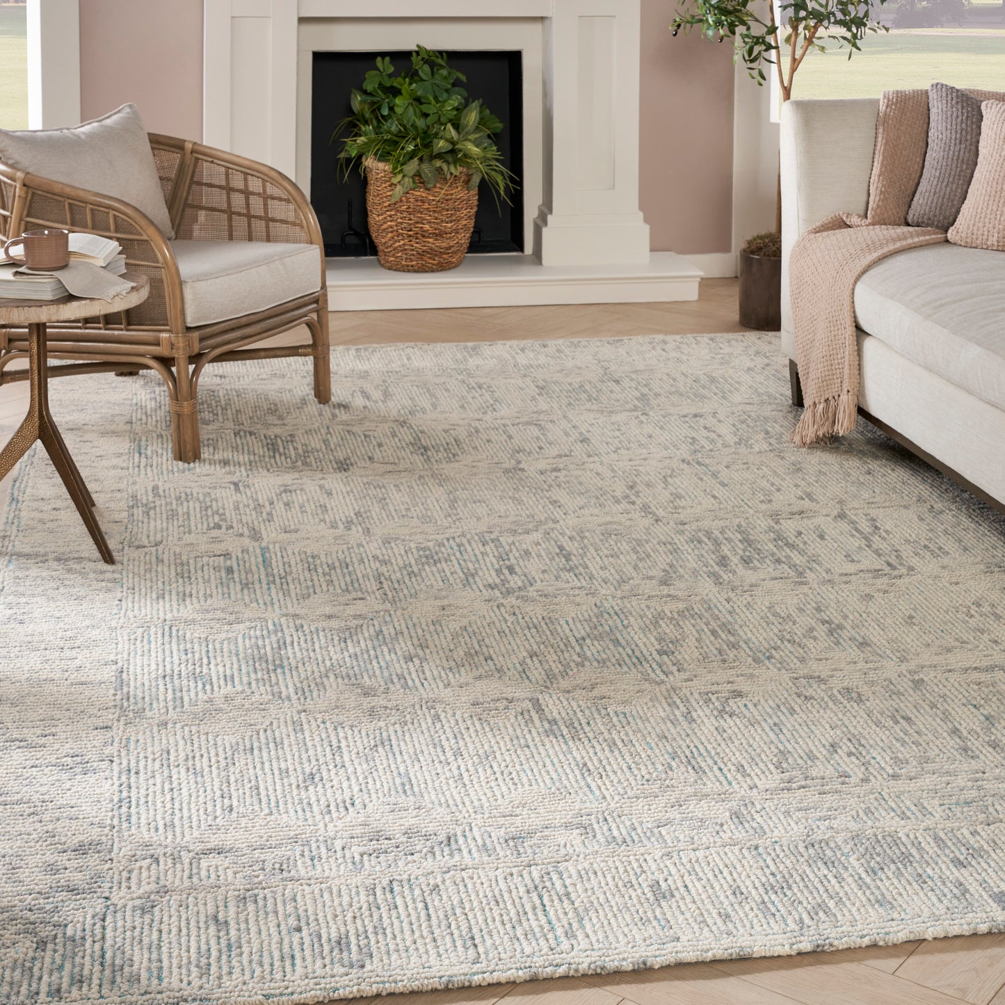 Soft blue-gray geometric area rug anchors a cozy living room with a beige sofa, rattan chair, and fireplace.