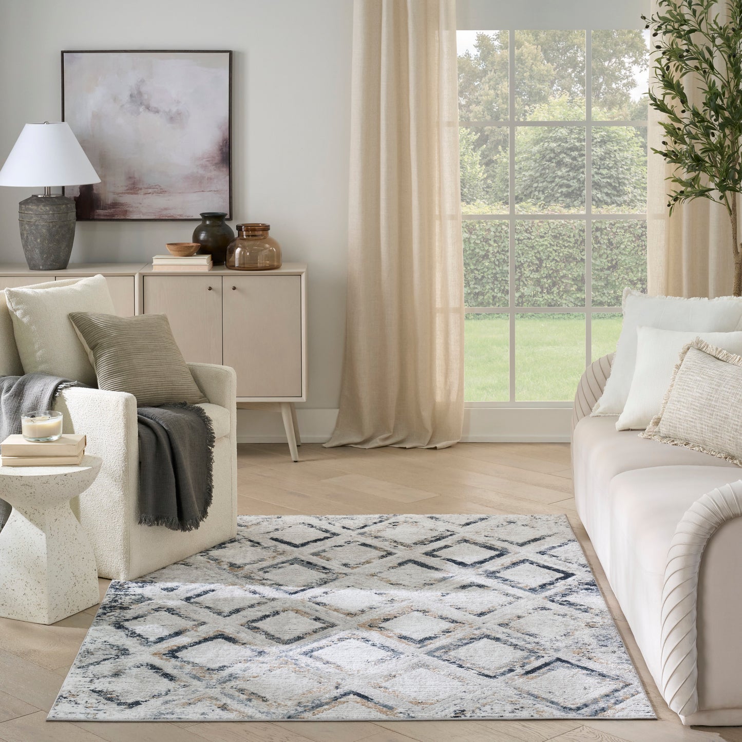 Neutral living room with cream sofa, textured throw, blue-gray diamond-pattern rug, beige drapes, and a light wood sideboard.