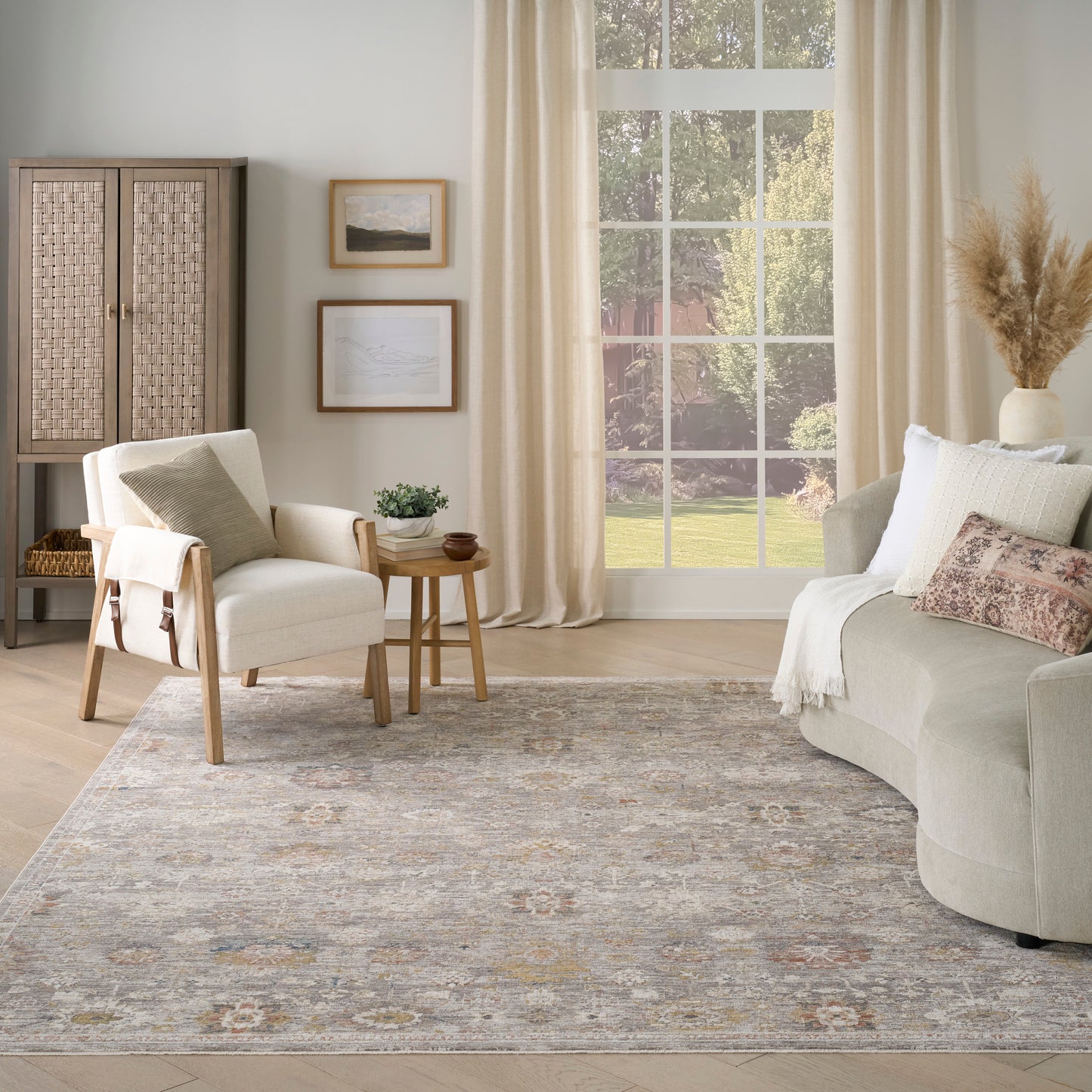 Neutral living room with beige sofa and armchair, wooden side table, woven cabinet, art, large window, rug, pampas decor.