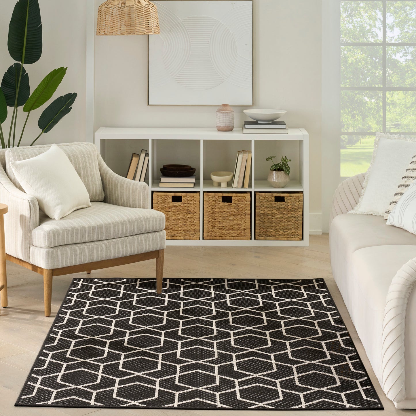 Boho living room with black and white geometric rug, cream armchairs, white cubby storage with wicker baskets, green plant.