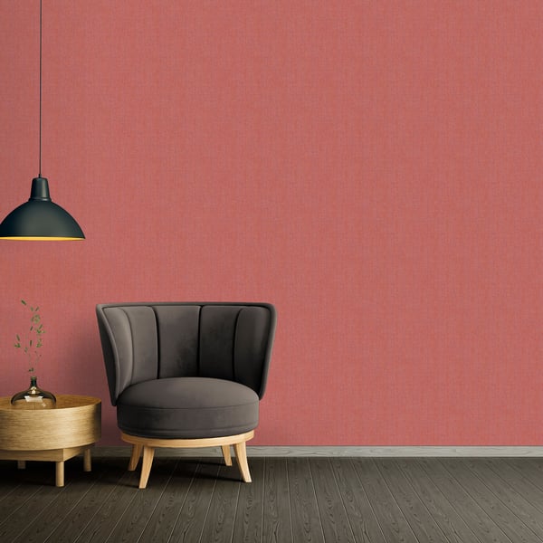 Red Hessian-effect textured wallpaper backdrop in a room with a dark gray curved lounge chair on light wood legs beside a round wooden side table under a black pendant lamp.