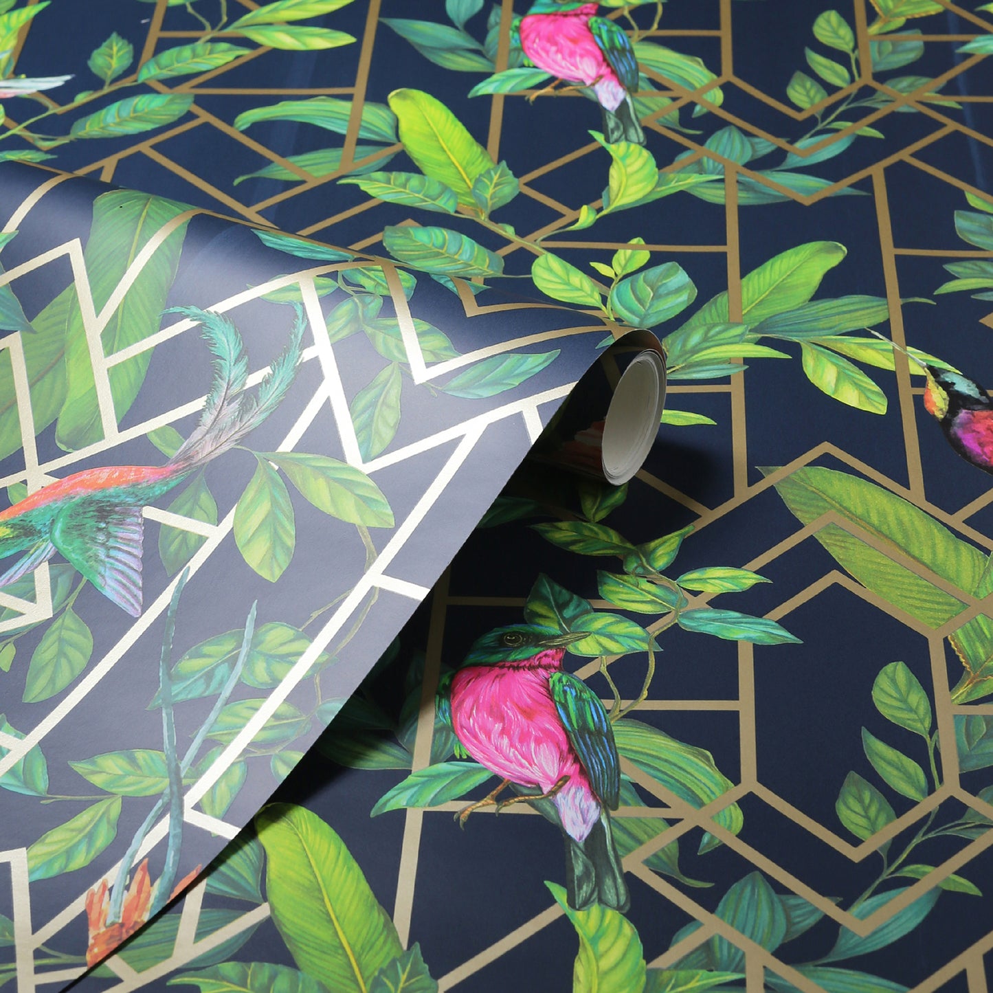 Tropical wallpaper with dark blue background, gold geometric lattice, green leaves and pink parrots; rolled sample.