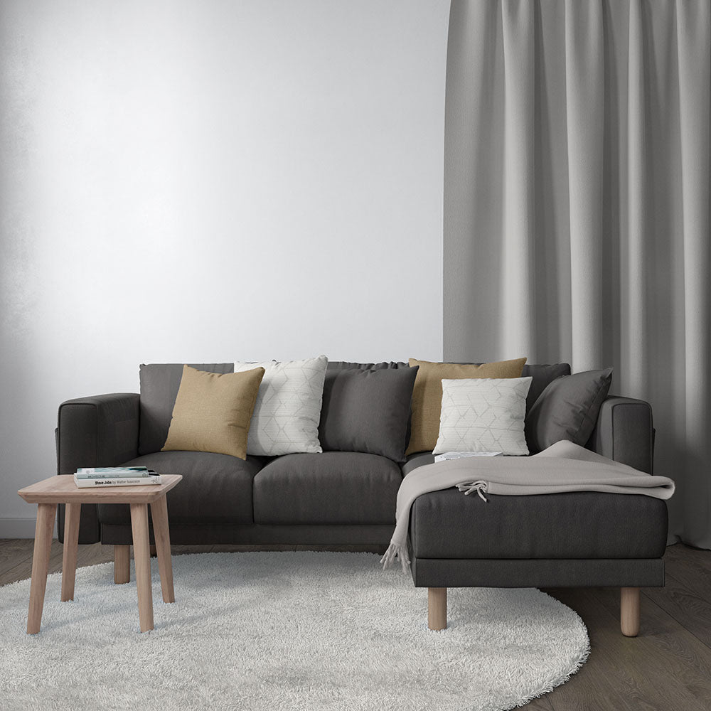 Dark gray L-shaped sofa with mustard and white cushions, light gray throw, wooden legs; round wood side table and gray rug.