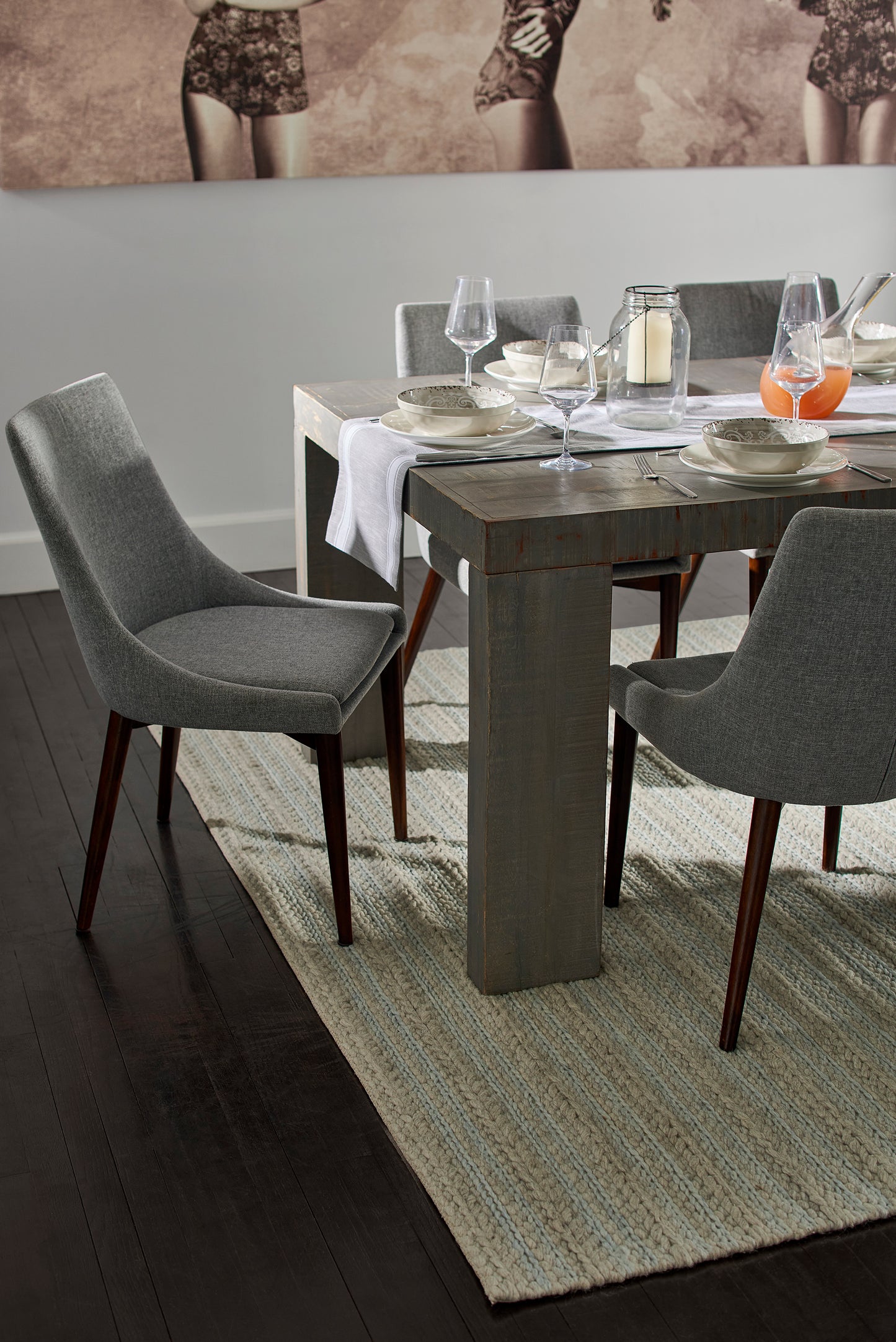 Grey upholstered dining chairs with wooden legs around a rustic dark wood dining table; set with plates, glassware, and candles.