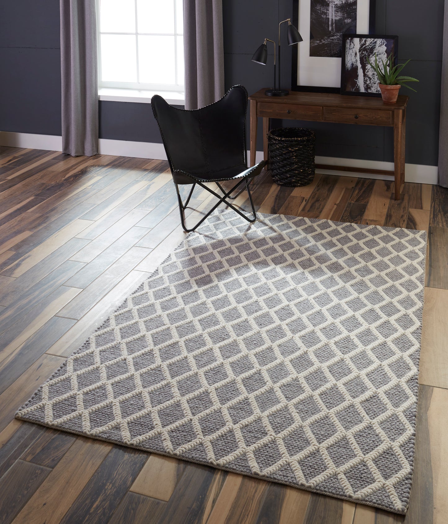 Rectangular grey and ivory diamond-lattice area rug on wood floor; modern living room with black butterfly chair and wooden desk.