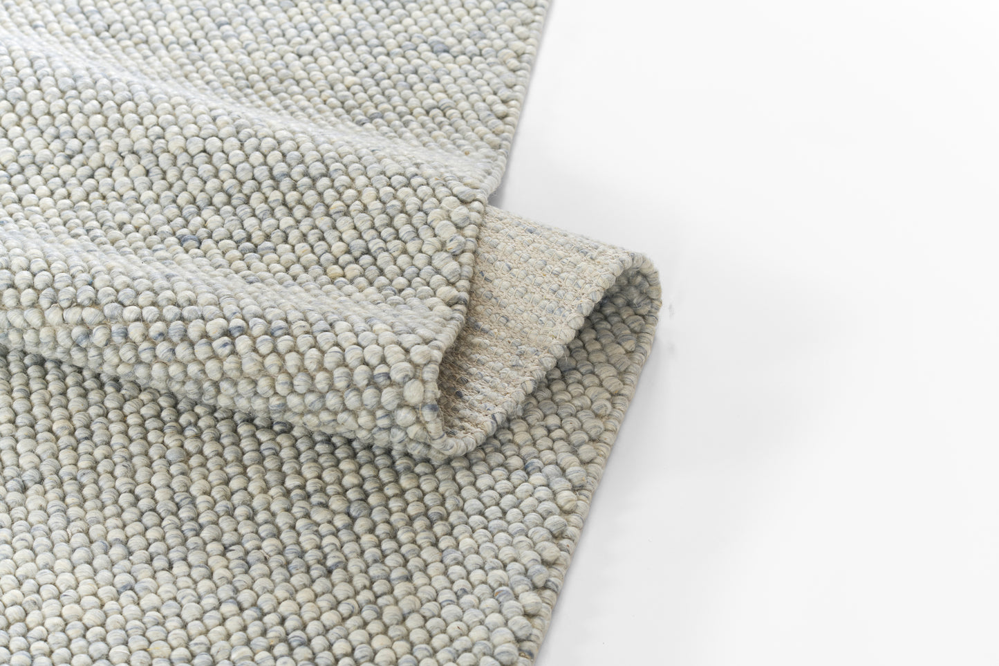 Soft boucle woven rug in pale grey-blue tones with a dense loop texture and folded edge.