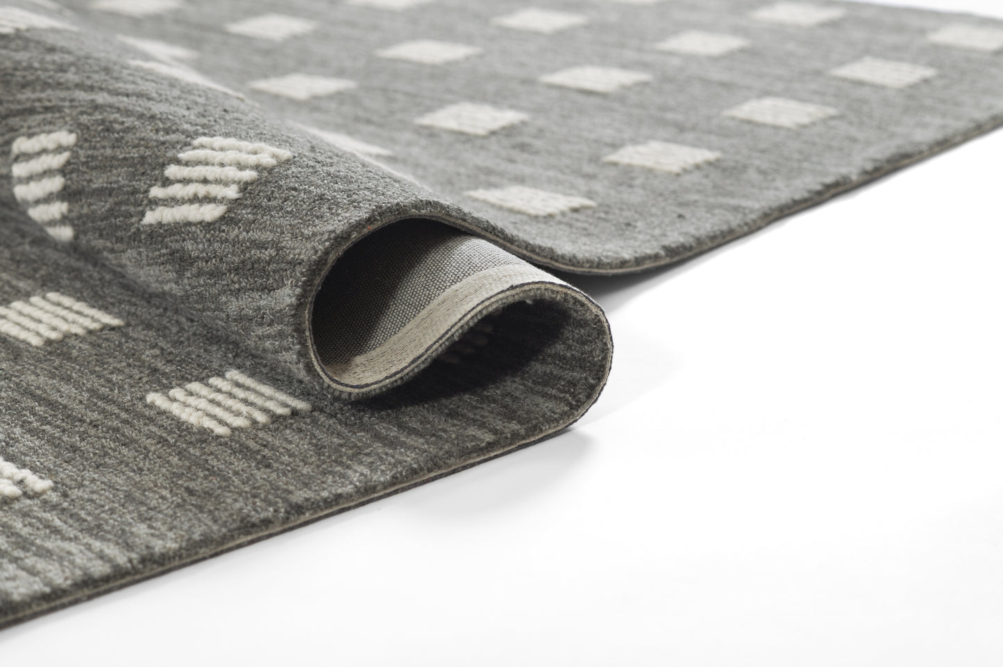 Gray area rug with white diamond pattern, plush pile, curled edge showing backing.