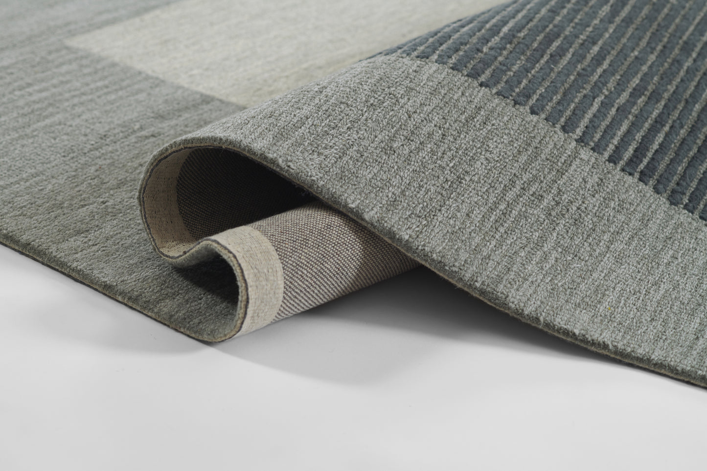 Grey-blue rug with ribbed texture and darker stripes; rolled edge reveals beige underside.