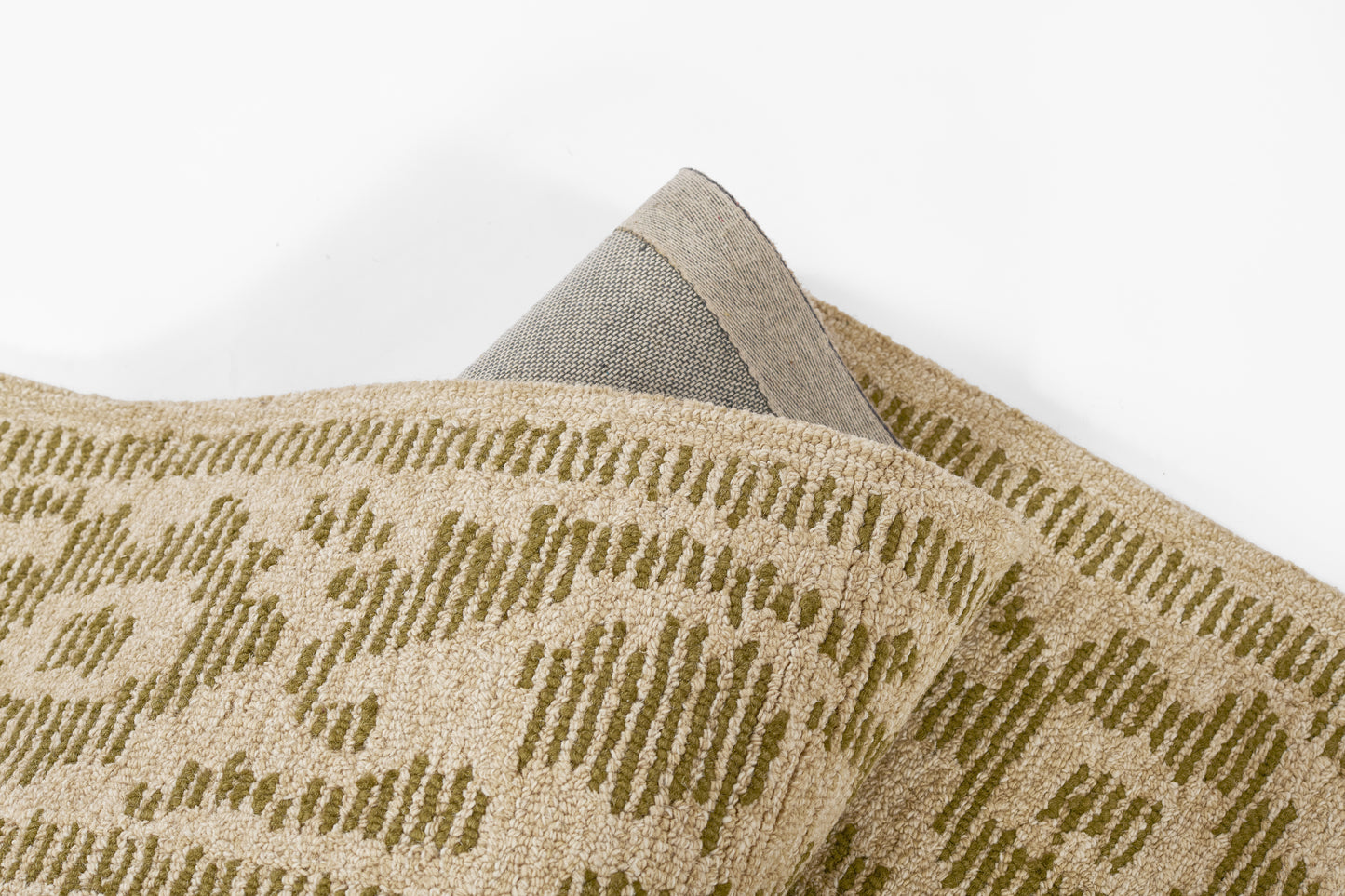Beige woven rug with olive green geometric pattern, rolled corner revealing grey underside.